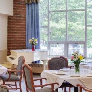 A bright dining area with a piano, tables set for a meal, and large windows letting in natural light.