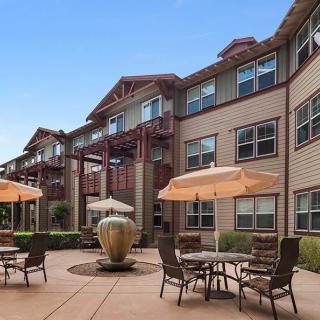 A view of a residential building with a patio area featuring tables, chairs, umbrellas, and a fountain.