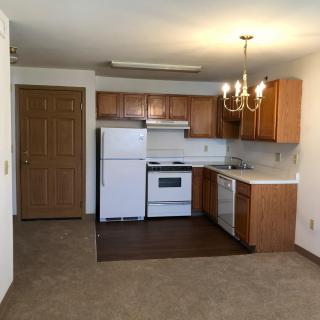 An apartment kitchen with wooden cabinets, featuring a refrigerator, stove, and dishwasher.