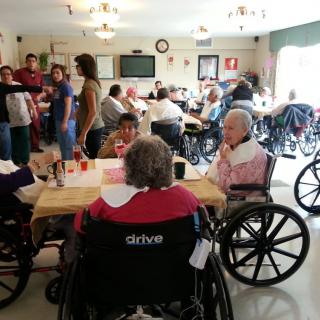 Elderly individuals in wheelchairs gathered in a communal room at a nursing home.