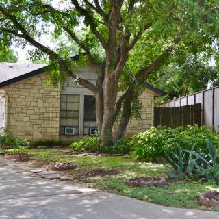 A cozy residential house with a stone exterior, surrounded by lush greenery and a spacious driveway.