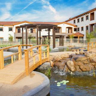 A serene courtyard featuring a pond with a wooden bridge and surrounding buildings.