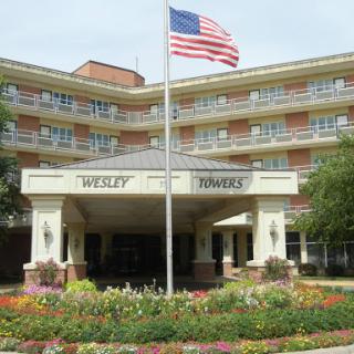 The entrance of a hotel, featuring an American flag and landscaped flowers.