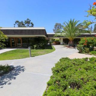 A sunny view of a building surrounded by lush greenery and a well-maintained garden path.