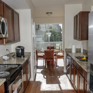 A modern kitchen with stainless steel appliances and wood cabinets opens into a sunlit dining area.