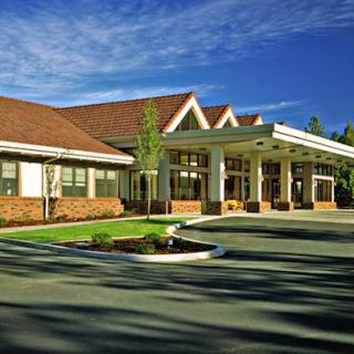 A welcoming entrance of a hospitality building, surrounded by well-maintained landscaping under a clear blue sky.