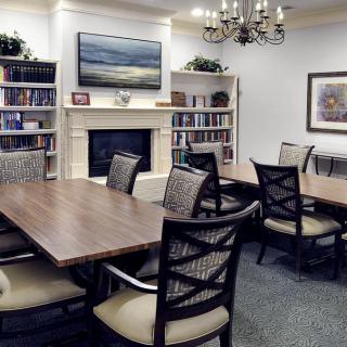 A cozy conference room with a long wooden table, surrounded by chairs and featuring a fireplace, bookshelves, and decorative artwork.