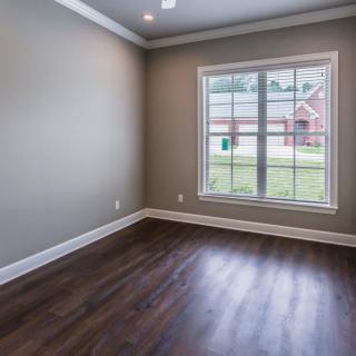 An empty room with wood flooring and a large window, allowing natural light to illuminate the space.