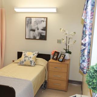 A cozy hospital room featuring a neatly made bed, bedside table with personal items, and decorative elements.