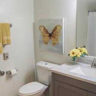 A bathroom with a butterfly painting, yellow towel, and floral decor.