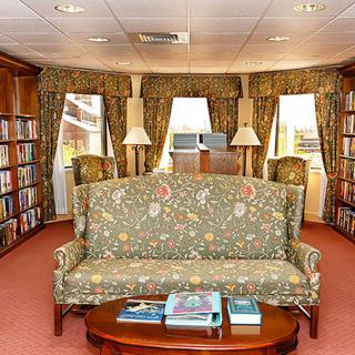 A cozy library interior with bookshelves, a patterned sofa, and reading lamps.