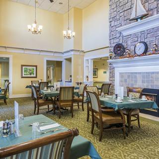A cozy dining room with neatly arranged tables and chairs, featuring a stone fireplace and nautical decor.