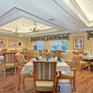A well-decorated dining room with multiple tables and chairs, featuring elegant lighting and large windows.