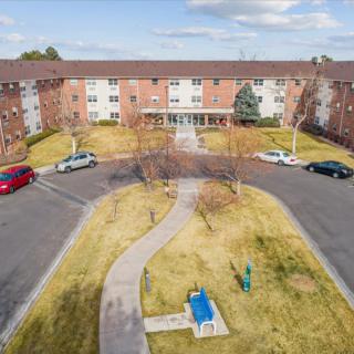 Aerial view of a brick apartment building with a circular driveway and parked cars.