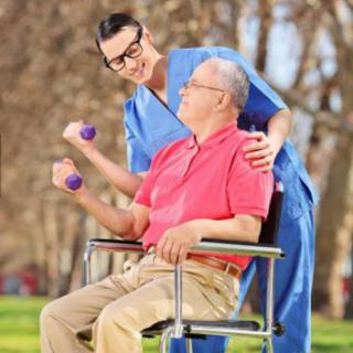 A caregiver encourages an elderly man in a wheelchair to exercise with light weights in a park setting.