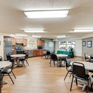 A spacious community dining area with multiple tables and chairs, adjacent to a modern kitchen.