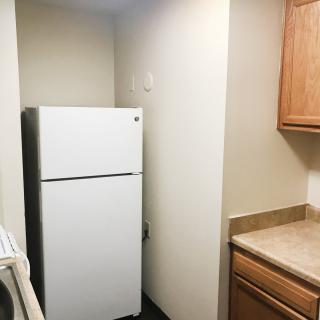 A compact kitchen space featuring a white refrigerator snugly placed between walls, with wooden cabinets and countertops.