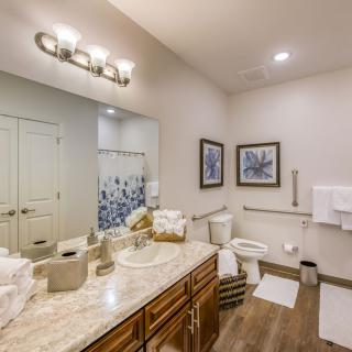 A modern bathroom with elegant decor, featuring a large mirror, sink, toilet, and shower with a decorative curtain.