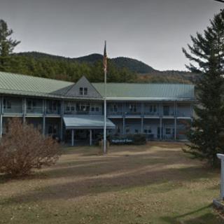 A historic hotel building set against a backdrop of mountains and surrounded by trees.