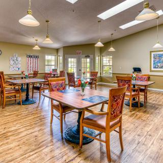 A dining area with wooden tables and chairs, well-lit by ceiling lights and natural light.