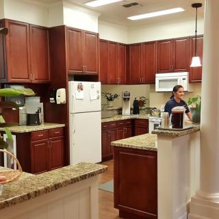 A modern kitchen with wooden cabinets, granite countertops, and a person standing near the sink.