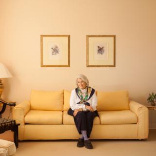 An elderly woman sitting on a sofa in a well-decorated living room.