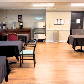 A spacious and simple dining area with neatly arranged tables and chairs, featuring a coffee station in the background.