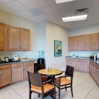 An office break room with wooden cabinets, a round table, and chairs, featuring a water cooler and coffee station.