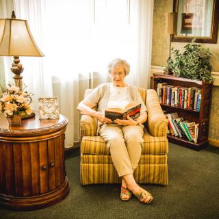 An elderly woman sits comfortably in a cozy room, reading a book.