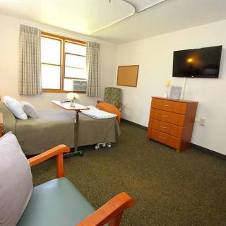 A clean and organized hospital room with a bed, chair, and mounted television.