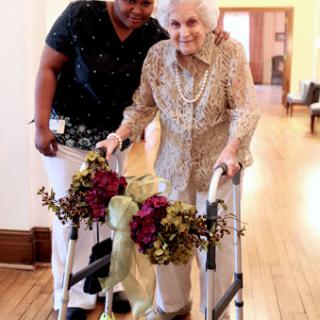 An elderly woman receiving support while using a walker, highlighting the importance of care and companionship.
