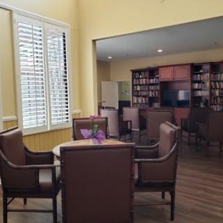 A cozy library seating area with chairs, a table, and bookshelves in the background.