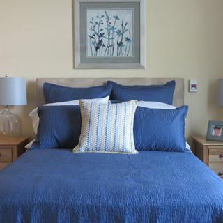 A neatly made bed with blue bedding and decorative pillows, accompanied by bedside tables, lamps, and framed artwork above the headboard.