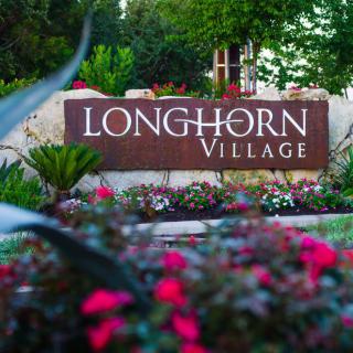 A welcoming sign for Longhorn Village surrounded by a vibrant garden.