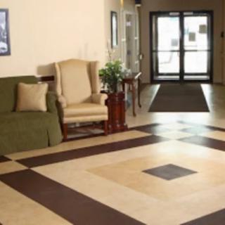 A spacious lobby area featuring a patterned floor, sofa, armchair, and entrance doors.