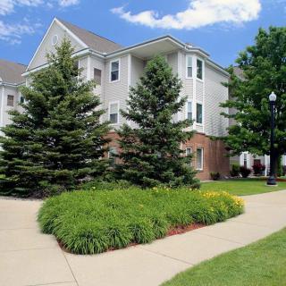 A suburban apartment building surrounded by well-maintained landscaping and a sidewalk.
