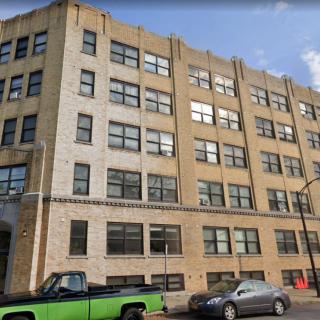 A multi-story brick building with parked cars on the street.