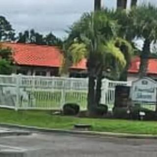 A fenced property with palm trees and a building in the background under a cloudy sky.