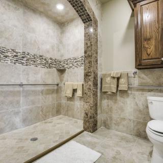 A modern bathroom featuring a tiled shower area, toilet, and wooden cabinet.
