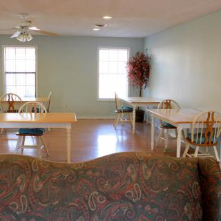 A cozy dining area with tables and chairs, featuring wooden flooring and a potted plant by the wall.