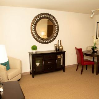A cozy living room with a mirror above a dark wood cabinet, accompanied by chairs and a table.