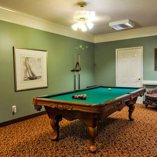 A cozy billiards room featuring a classic pool table in the center, surrounded by green walls and complemented by elegant artwork.