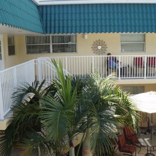 A sunny courtyard with a balcony, tropical plants, and outdoor seating.