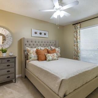 A cozy and well-decorated bedroom featuring a bed with plush pillows, a stylish mirror above a dresser, and elegant curtains filtering the light.