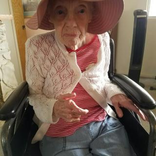 An elderly woman wearing a hat and sitting in a wheelchair indoors.