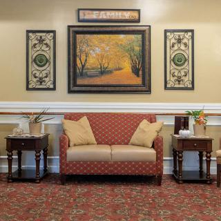 A cozy living room with a red patterned sofa, artwork on the wall, and side tables.