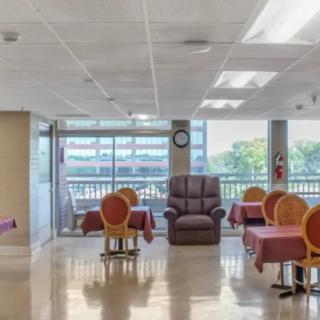 A bright indoor space with tables, chairs, and a view of the outside through large windows.