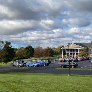 A parking lot with several cars in front of a building under a cloudy sky.