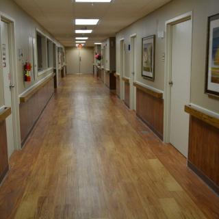 A long, well-lit hallway with wooden flooring and multiple doors.