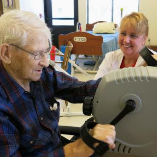 An elderly man engages in exercise with the support of a healthcare professional, promoting physical rehabilitation.